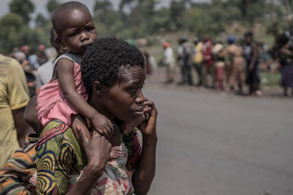 A woman carries her baby on the back as they flee Masisi territory following clashes between M23 rebels and government forces.