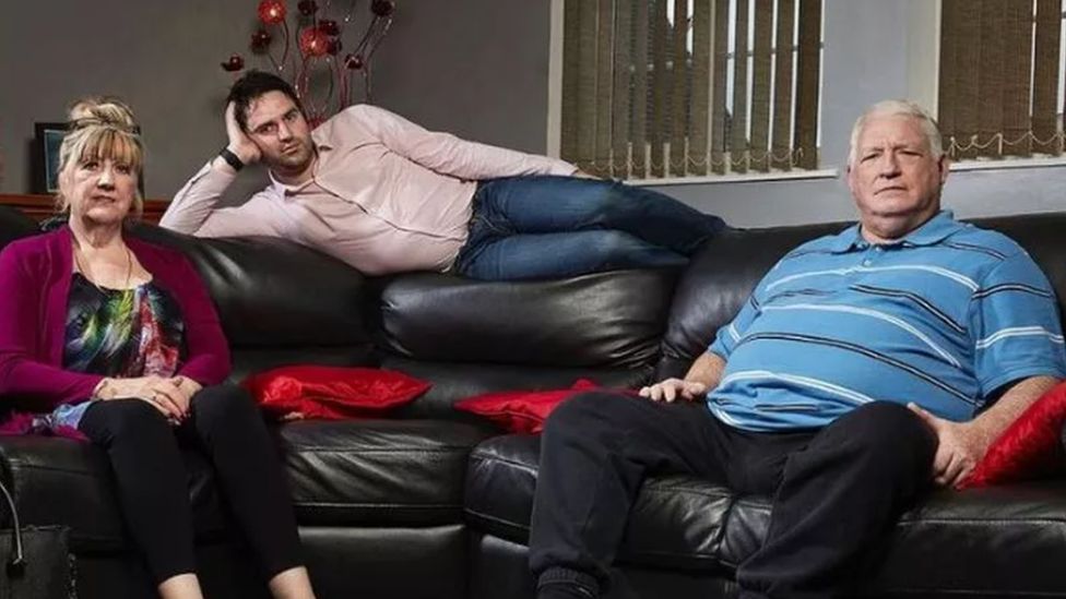 George Gilbey, his mother Linda and late stepfather Pete, sitting on a black sofa