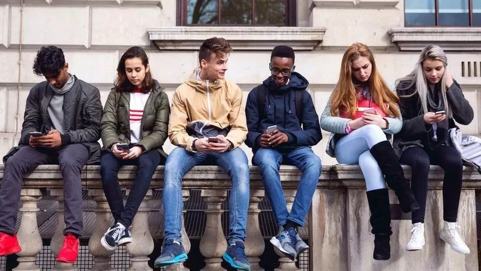 Young people sat on a wall on mobile phones