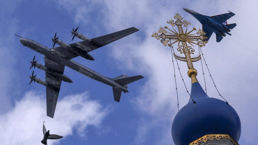 A Russian Su-35S combat aircraft and a Tu-95ms strategic bomber fly in formation above a church during a rehearsal for the flypast,
