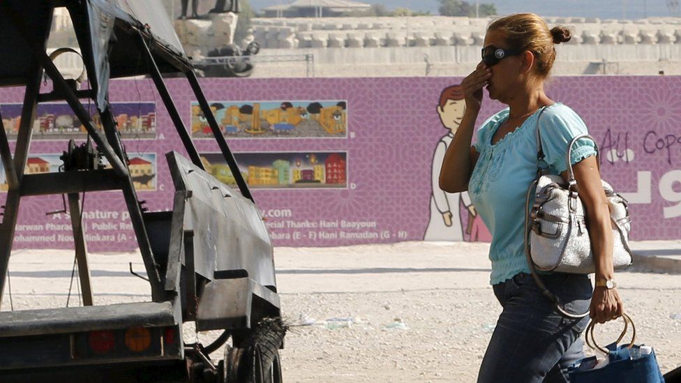 A woman holds her nose as she walks past a burnt-out police vehicle in central Beirut (24 August 2015)