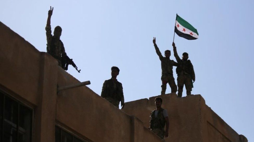 Turkish-backed Syrian fighters wave the Syrian opposition flag on top of a building in the south-western neighbourhoods of the border town of Tal Abyad on 13 October 2019