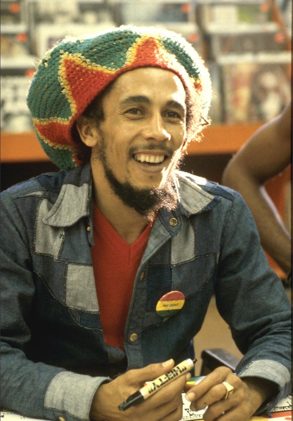 Bob Marley sits at a table holding a pen