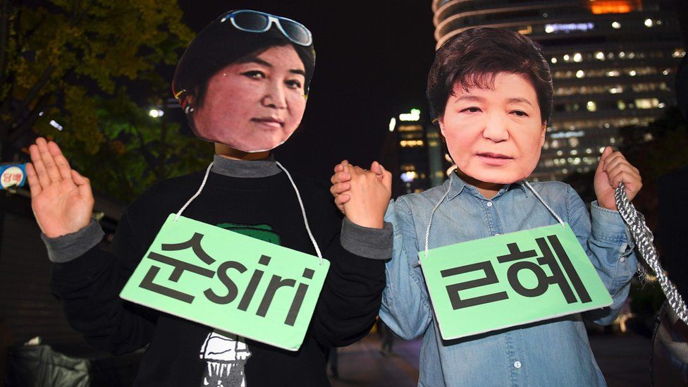 Protestors wearing masks of South Korean President Park Geun-Hye (R) and her confidante Choi Soon-Sil (L) pose for a performance during a rally denouncing a scandal over President Park"s aide in Seoul on October 27, 2016