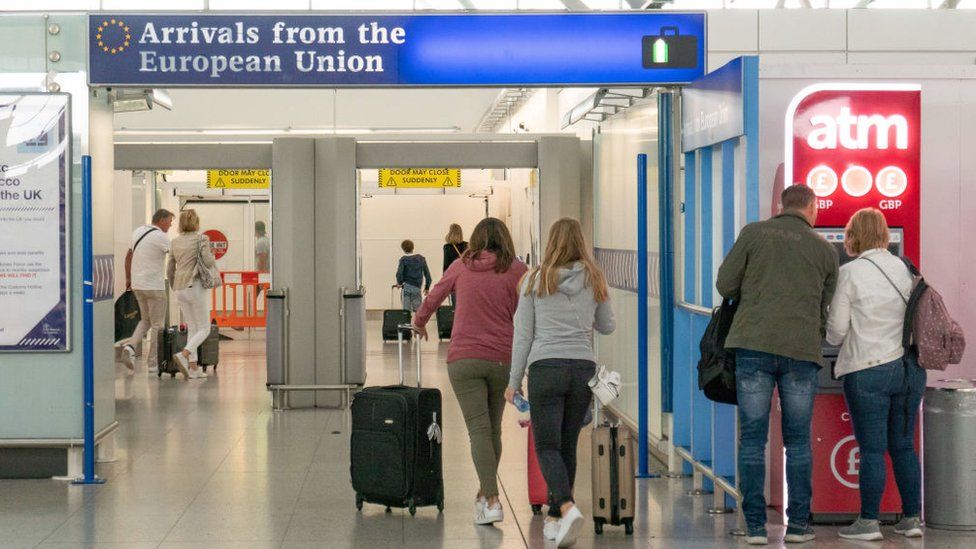 People at an airport walking under a sign saying "arrivals from the European Union".