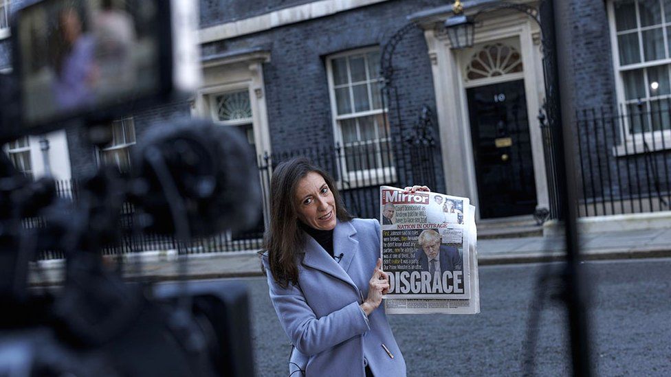 A TV presenter holds a copy of a newspaper outside 10 Downing Street on 13 January 2022