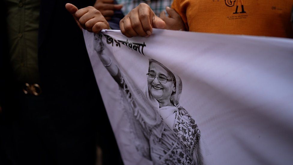 People's hands holding a cloth with an image of Sheikh Hasina on it
