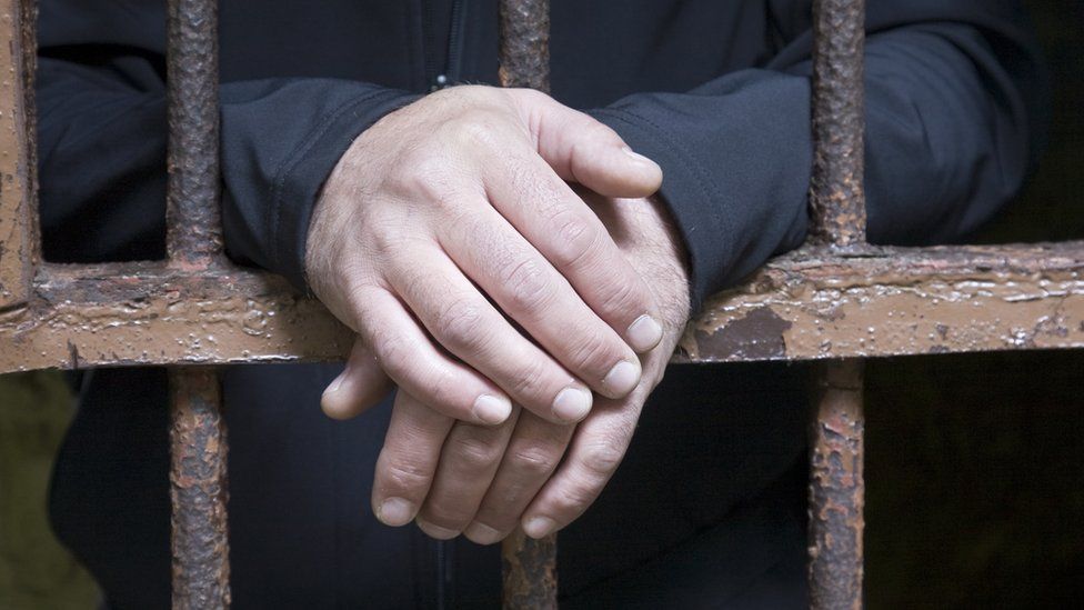 Man's hands behind jail bars