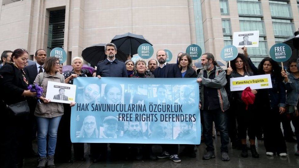 People outside Istanbul's court hold placards and a banner with pictures of the accused activists. Photo: 25 October 2017