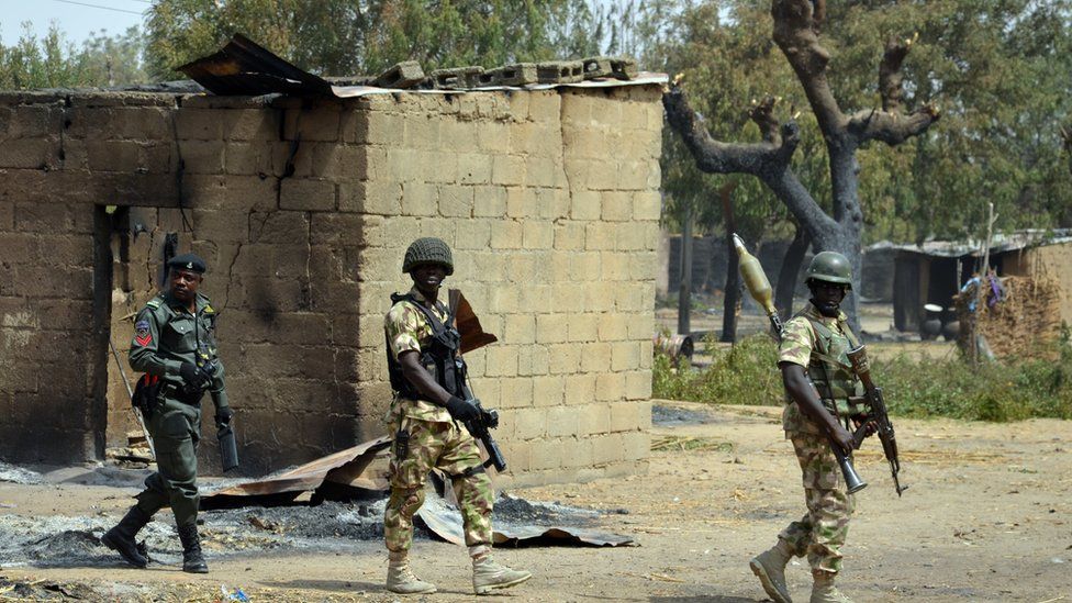 Soldiers and policemen walk past burnt house on 4 February 2016 during a visit to the village of Dalori village, Borno state, after Boko Haram attack