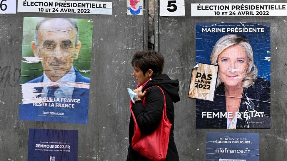 A pedestrian walks past campaign posters of French far-right party Reconquete! presidential candidate Eric Zemmour (L) and French far-right party Rassemblement National (RN) presidential candidate Marine Le Pen (R), three days ahead of the first round of the French presidential election, in Paris on April 7, 2022.