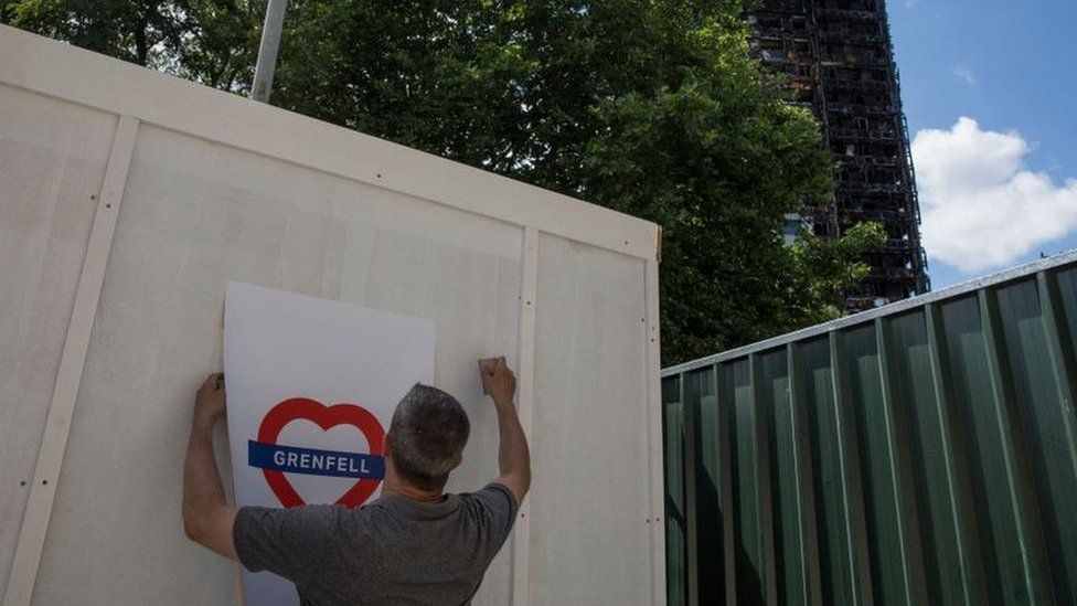man puts up heart shaped Grenfell poster in the shadow of the burnt out tower