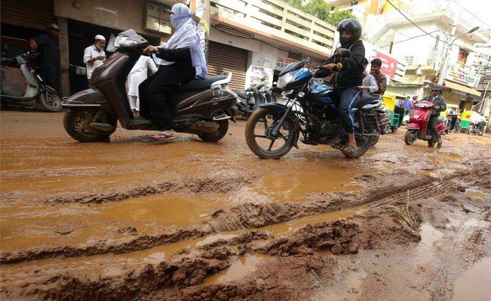 Indian cars, scooters, and motorists drive on a damaged road consists of water logged and potholes following recent heavy rains, in Bangalore, India, 12 October 2017