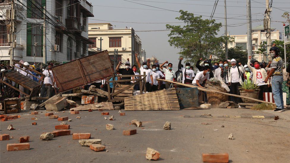 Demonstrators gesture at riot police behind makeshift barricades during a protest against the military coup in Mandalay