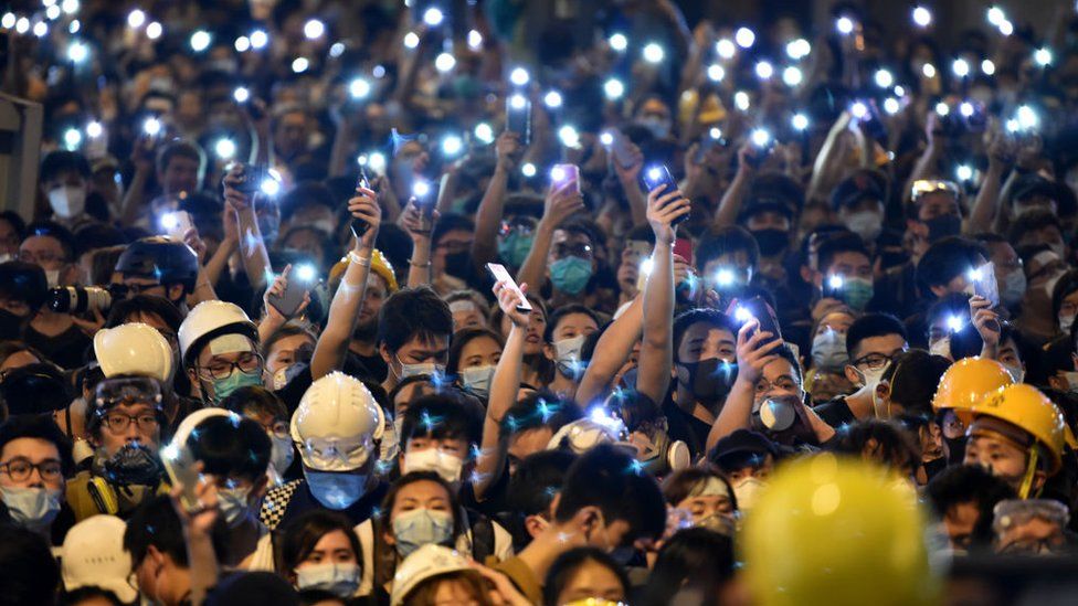 Protesters hold up their mobile phones as they gather outside the police headquarters in Hong Kong on 21 June