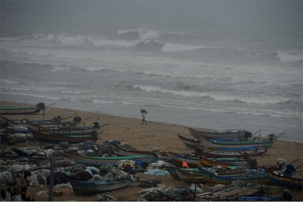An Indian fisherman walks near boats as waves break on the cost of the Bay of Bengal in Chennai on December01, 2016.