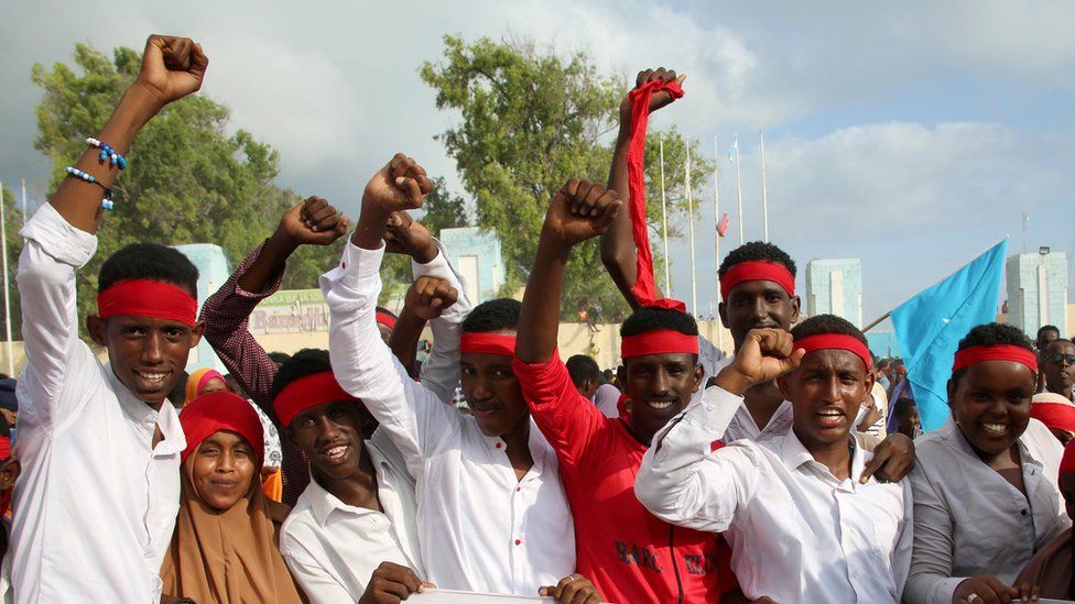 men in red bandanas and white shirts, raising their fists and smiling