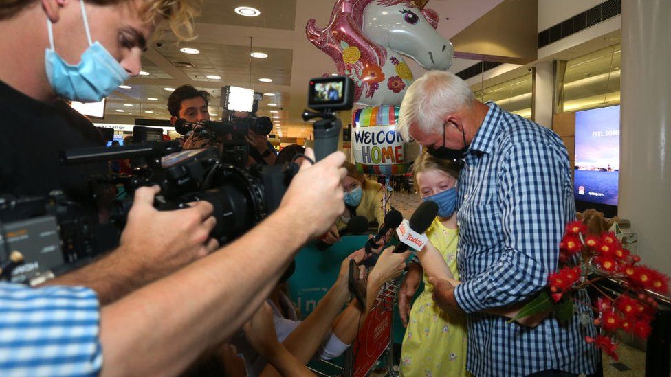 A girl hugs her grandfather after arriving in Sydney on Monday, as the media watches on