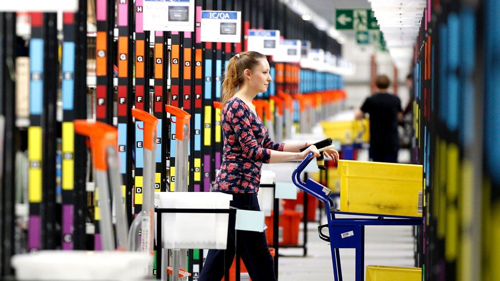 A worker collects items from storage shelves as she collates a customer order inside an Amazon fulfillment centre in Hemel Hempstead, north of London