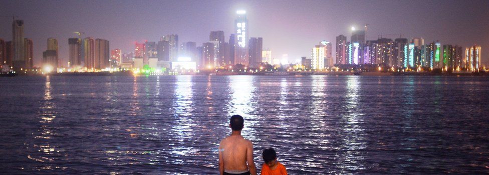 A man and child stand looking at the Wuhan skyline on the Yangtze River