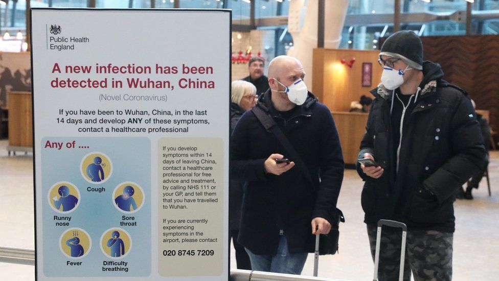 Passengers at Heathrow next to a coronavirus sign