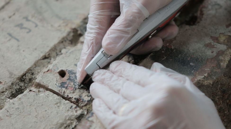 A restorer scrapes the bricks with a Stanley knife