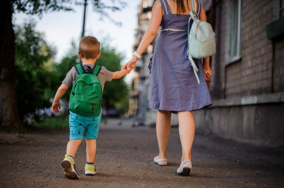 Woman and boy walk away holding hands