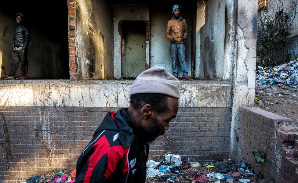 An unknown man walks past two others at the entrance to the derelict San Jose building in Johannesburg, South Africa