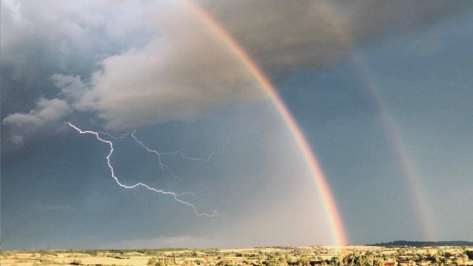 Forks of lightning by a double rainbow