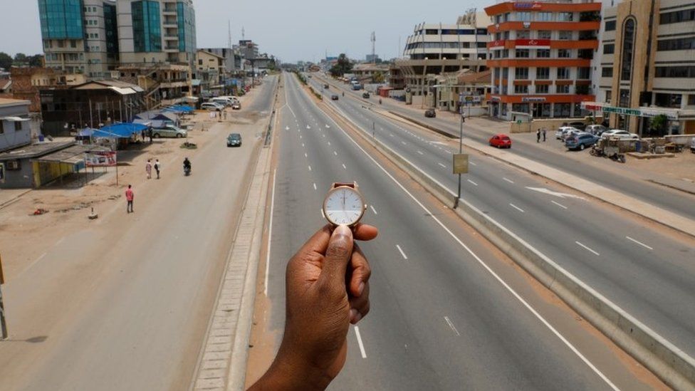 A watch showing the time at noon, is displayed for a photo as people walk past Ring Road Central Street, which is almost empty during the coronavirus disease (COVID-19) outbreak, in Accra, Ghana, March 31, 2020