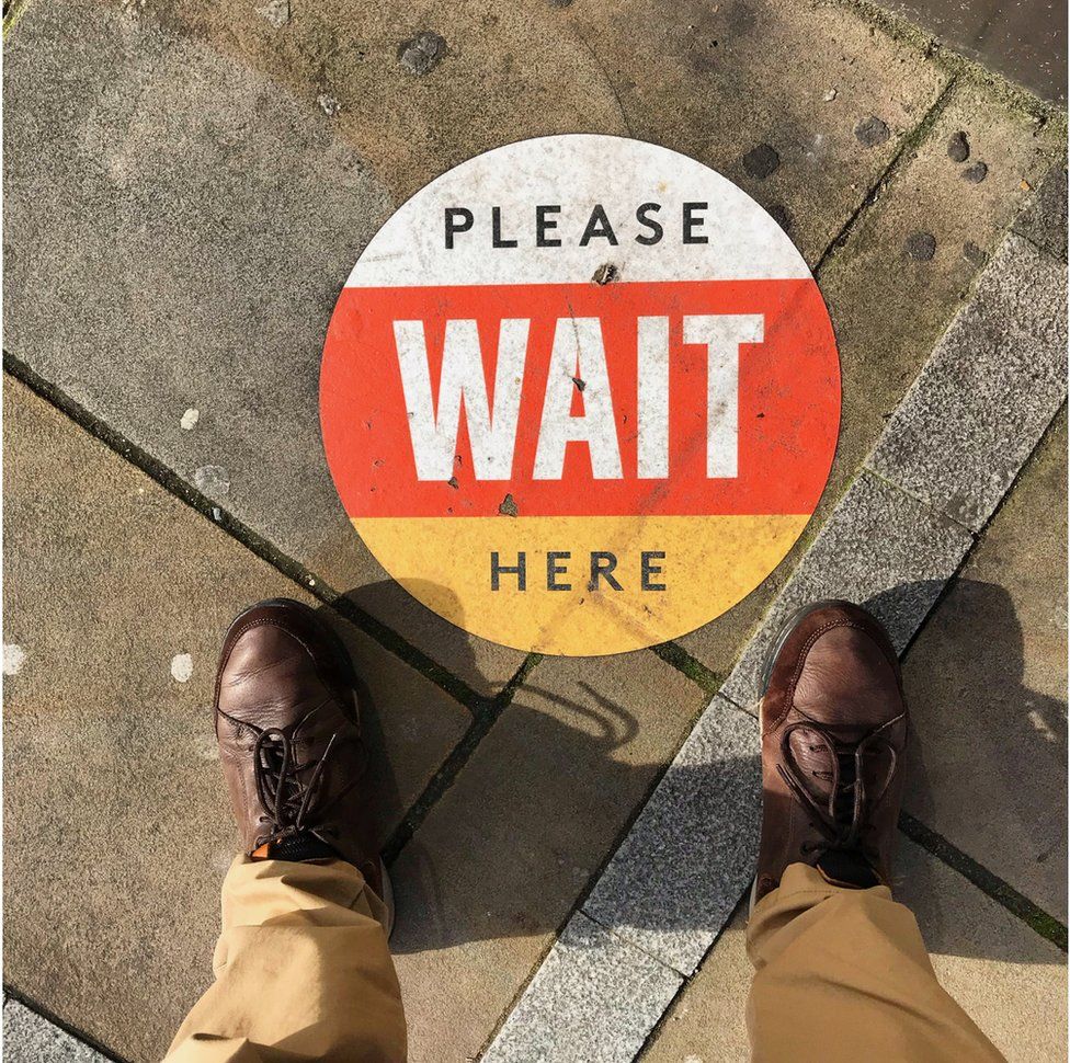 A sign on the ground instructing people to wait