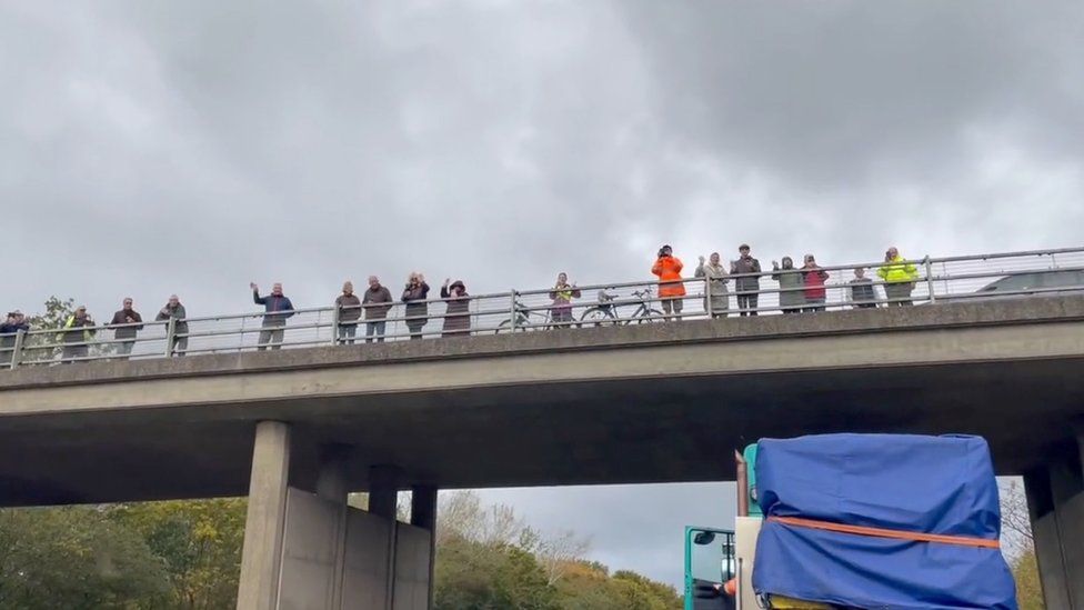 People gather on an overpass and wave at an abnormal load.