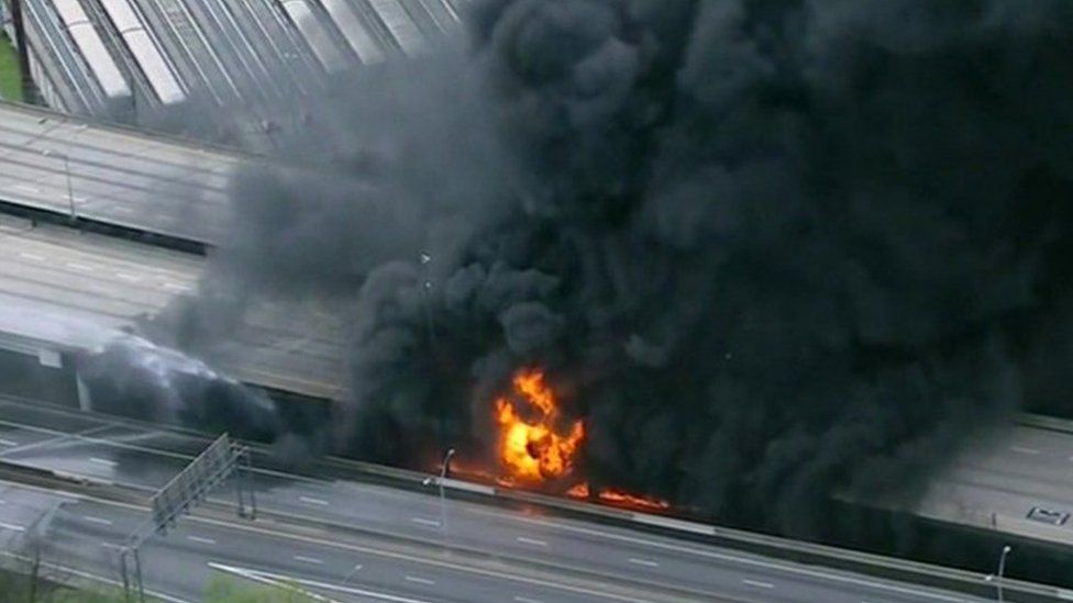 Aerial shot showing raging flames and plumes of black smoke on interstate 85