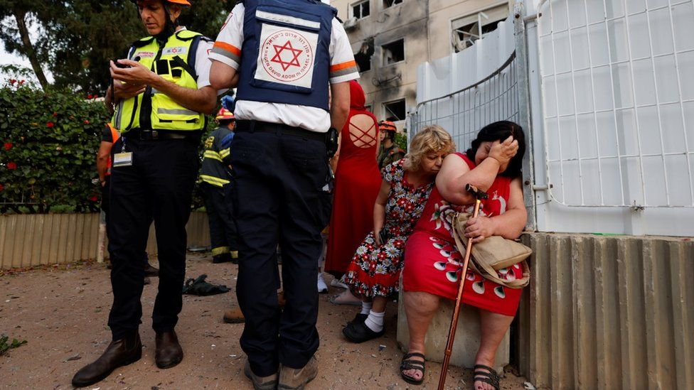 Israeli medics stand near women after a rocket hit a block of flats in Ashkelon, southern Israel (11 May 2021)