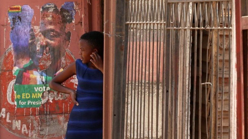 A girl looks on next to a defaced campaign poster of President Emmerson Mnangagwa in Harare, Zimbabwe - Monday 6 August 2018