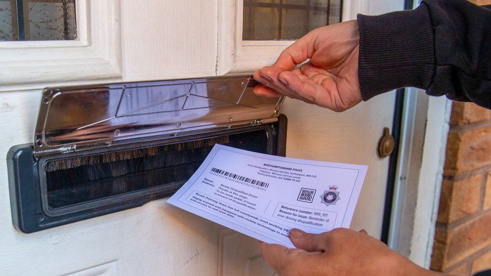A hand is visible pushing a printed postcard through a letterbox