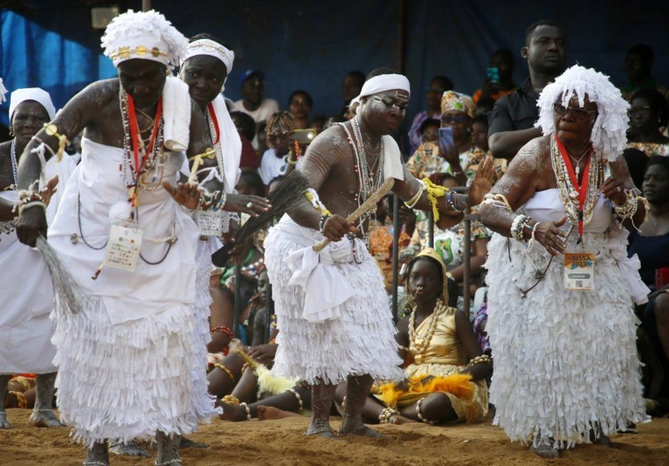 People dance wearing white, with white paint etched onto their arms and chests.