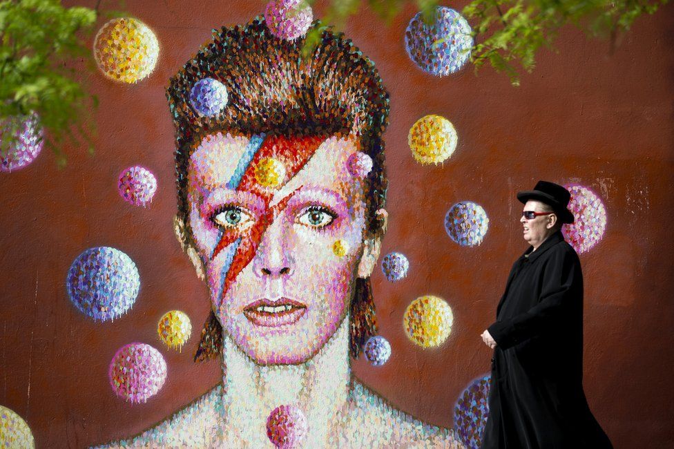 A man walks past a 3D wall portrait of British musician David Bowie, created by Australian street artist James Cochran, also known as Jimmy C, in Brixton, South London, on 19 June 2013. The artwork is based on the iconic cover for Bowies 1973 album, Aladdin Sane.