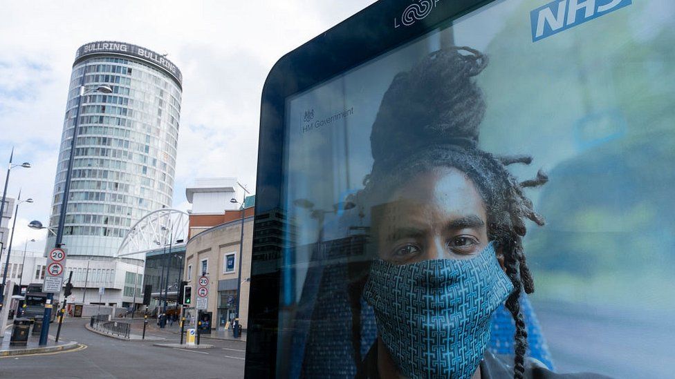 man with locs wearing face-mask on NHS poster
