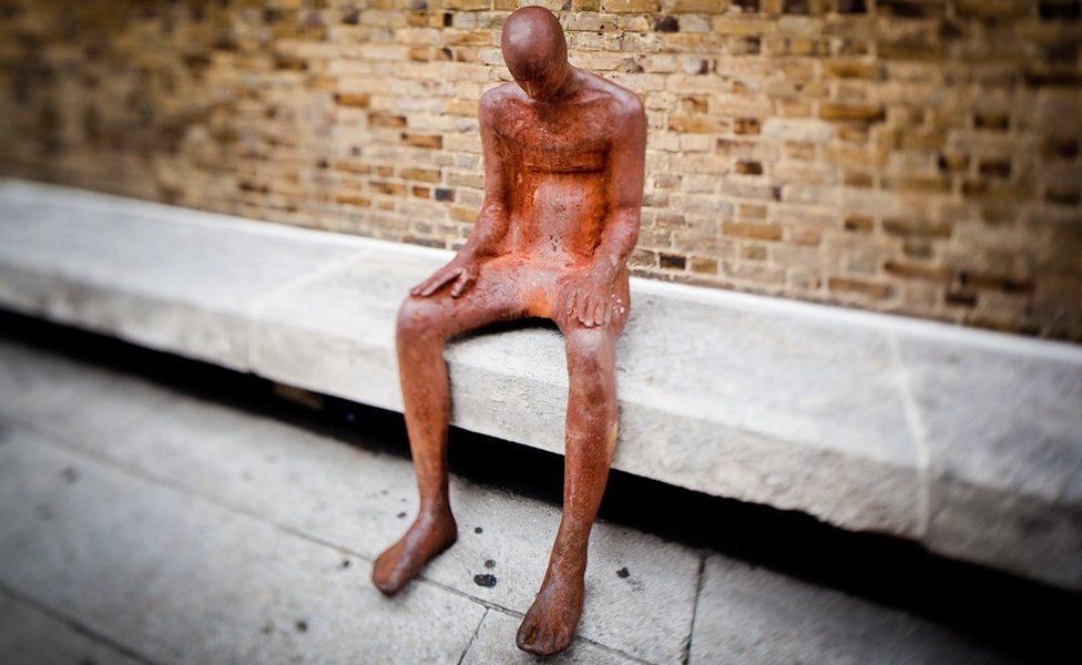 Life-sized sculpture sitting on a concrete bench