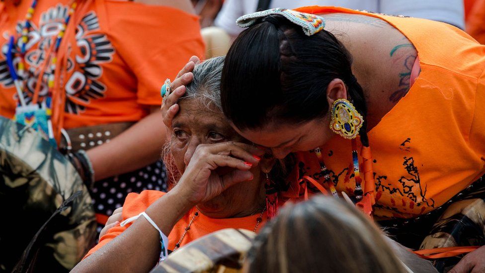 Indigenous women cry during a ceremony to mark the discovery of 750 unmarked graves at a Canadian residential school (1 July)