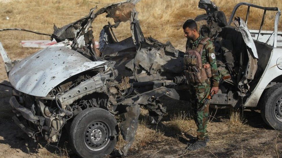 Iraqi militia fighter inspects the remains of a vehicle destroyed in an attack by IS militants that left 10 people dead in Mukaishefah, Iraq (3 May 2020)
