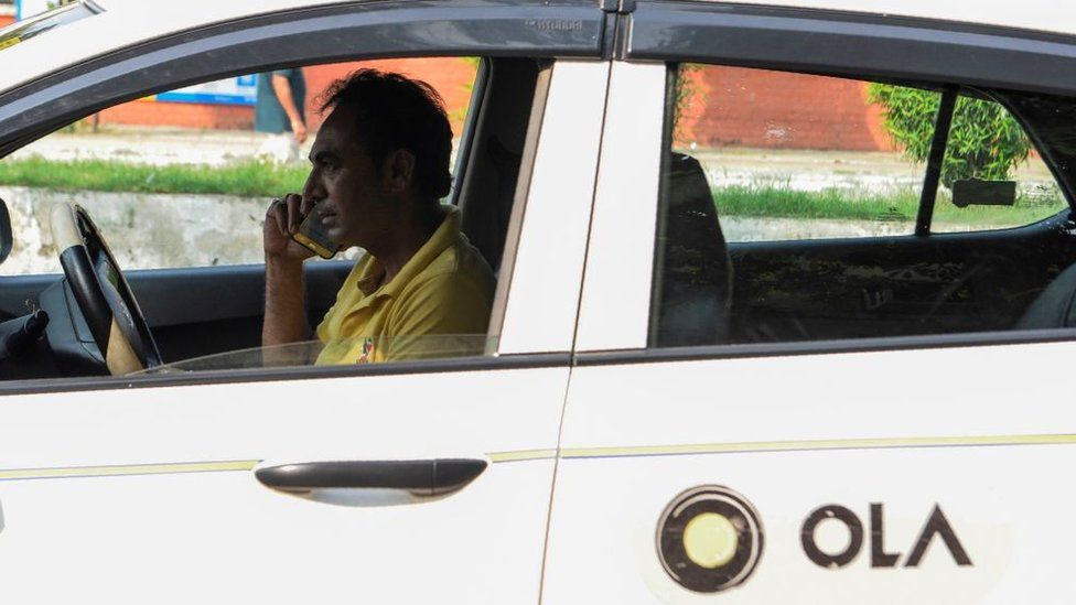 Водитель такси Ола разговаривает по мобильному телефону на обочине дороги в Амритсаре