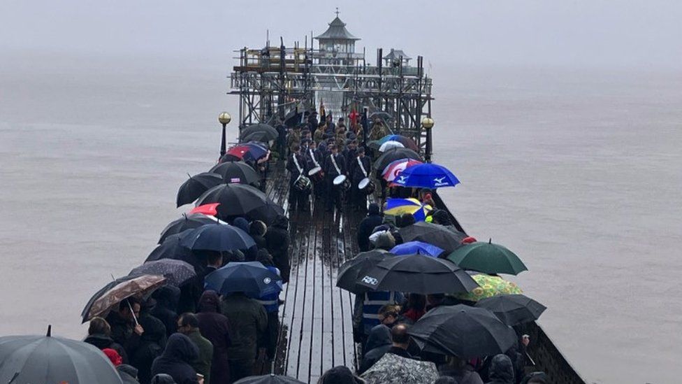 Clevedon Pier. Lots of people can be seen overlooking the water, holding umbrellas.