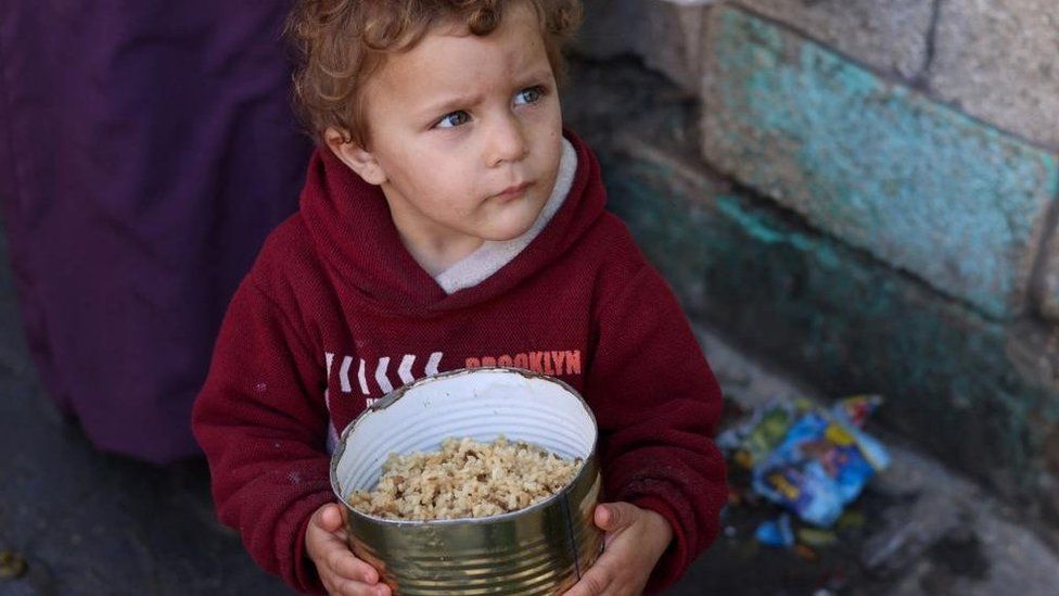 Palestinian boy holds container of food in Rafah (Feb 2024)