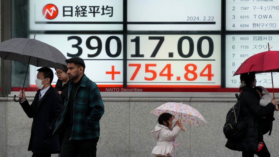 Pedestrians walk past a display showing the Nikkei Stock Average after surpassing the record closing of 38,915.87 points marked at the end of December 1989, during a morning trade session in Tokyo, Japan, 22 February 2024.