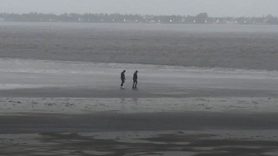 Two people walk on the exposed seabed after waters receded ahead of Hurricane Ian