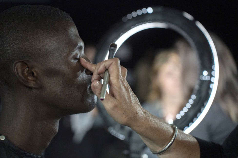 A make-up artist applies product to a man's eyelid.
