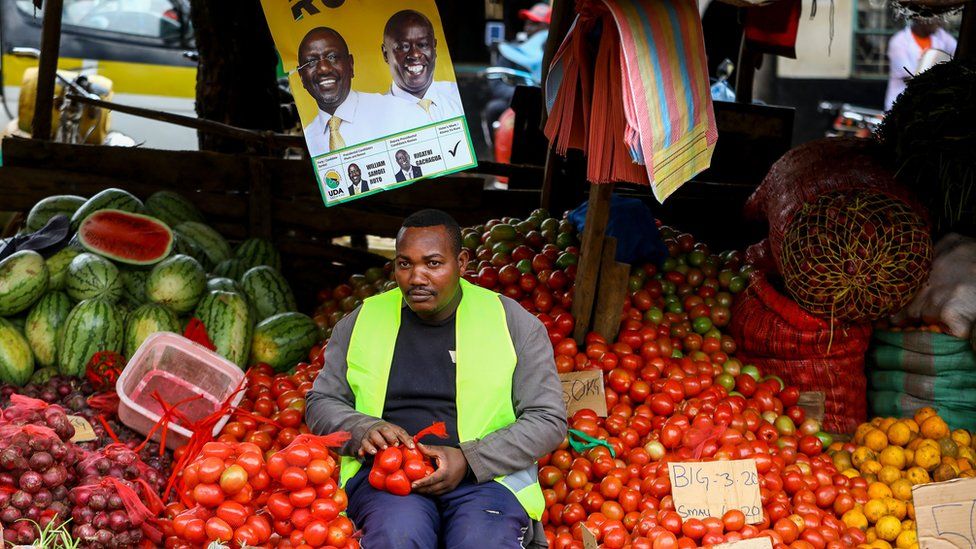 On Wednesday a supporter of the Kenya Kwanza Coalition sits amongst tomatoes under a poster of Ruto in Kangari, Kenya - Wednesday 28 July 2022