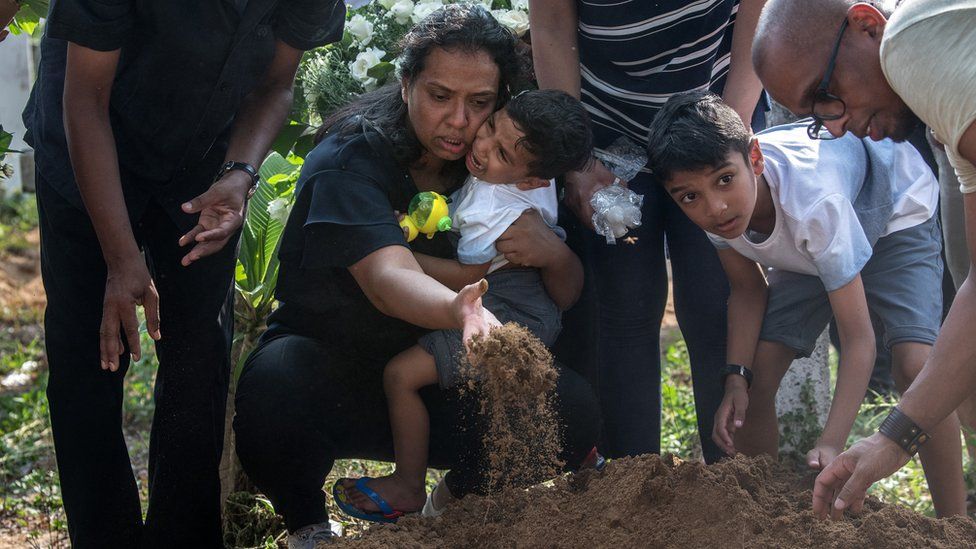 A woman holds a crying child as she throws earth onto a coffin during a funeral for a person killed in the Easter Sunday attack on St Sebastian"s Church, on April 23, 2019 in Negombo